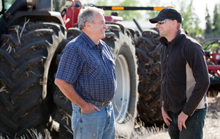 two men conversing in front of farm equipment