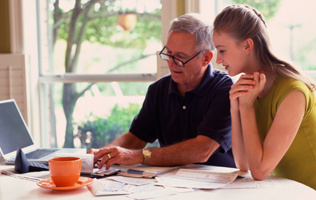 older man showing adult daughter how to balance a checkbook